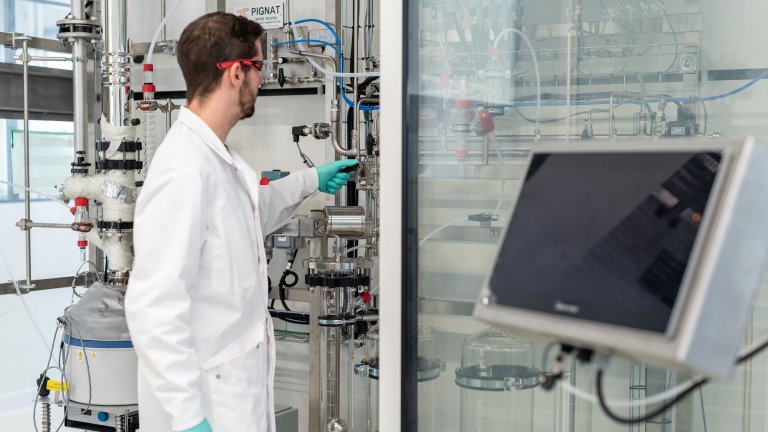 A lab technician operates equipment in a laboratory, adjusting a valve and monitoring a digital display