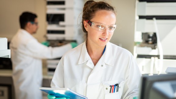 Image of woman in a white lab coat with protective goggles