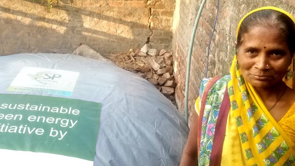 An Indian woman stands beside a large biogas bag, promoting a sustainable green energy initiative in her community
